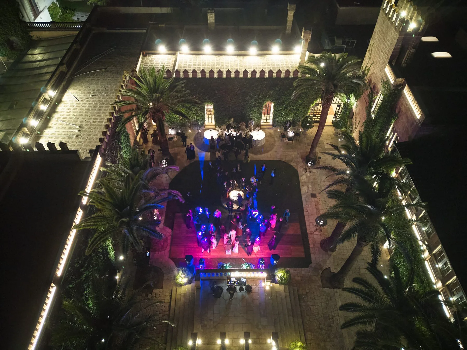 Vista aerea notturna della festa nel cortile illuminato di Castello Monaci