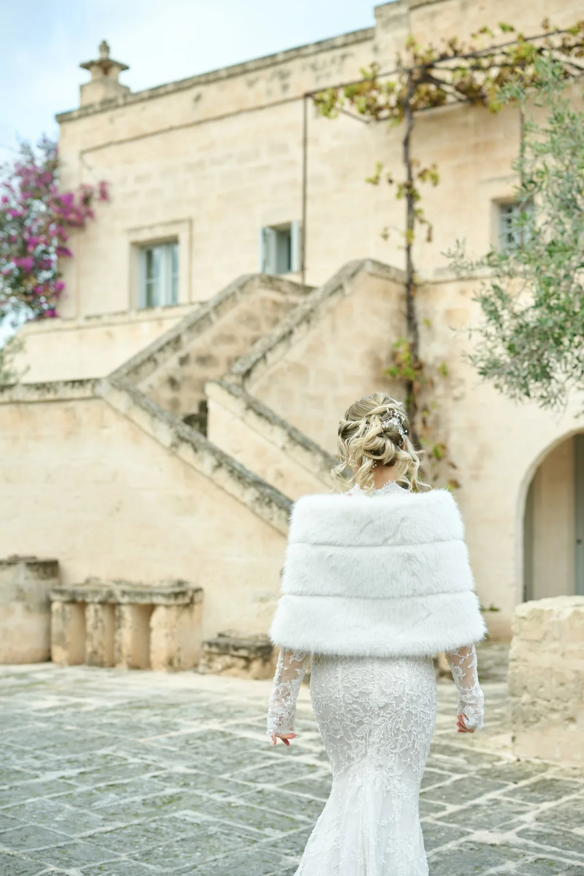 La sposa di spalle davanti alle scale e alle case in tufo