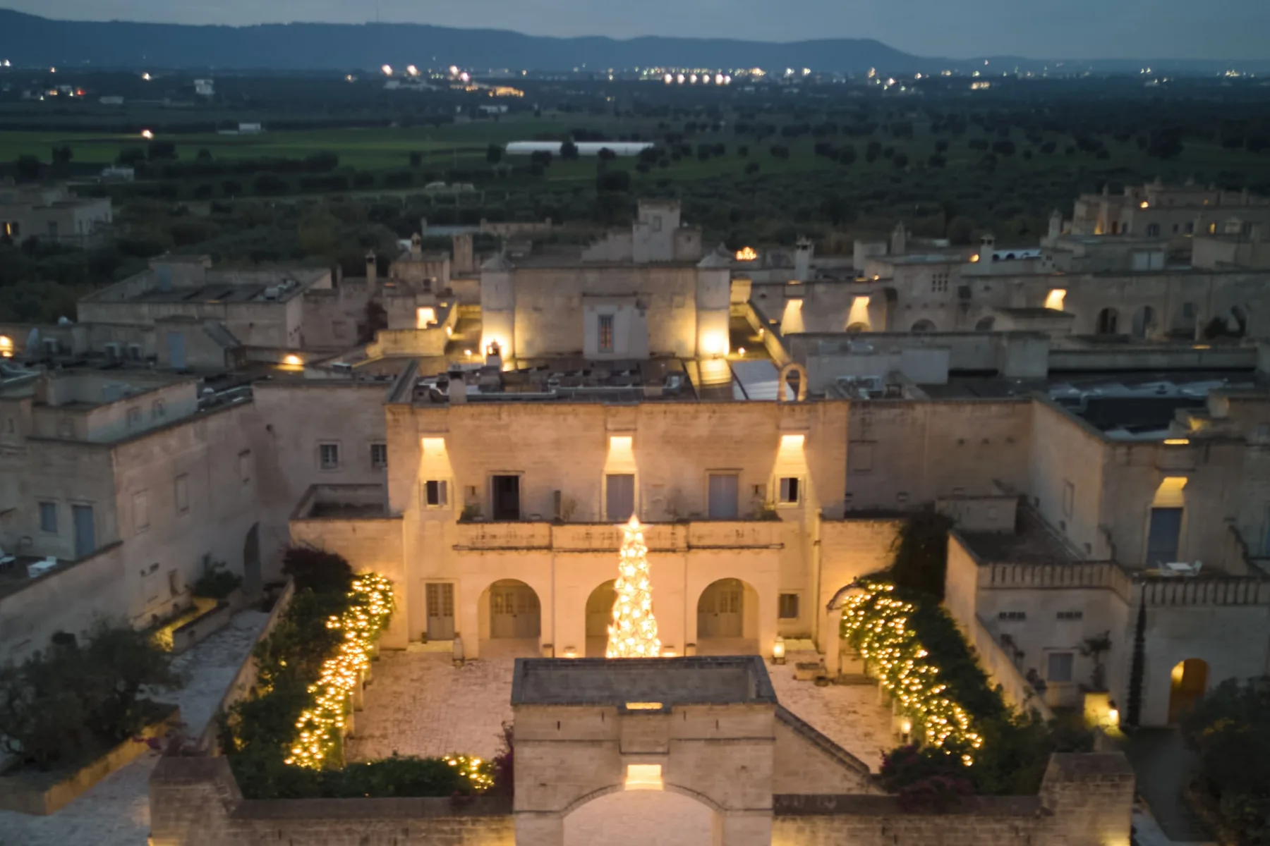 Borgo Egnazia illuminato al tramonto visto dal drone, con la piazza, l'albero di Natale e la campagna di Fasano