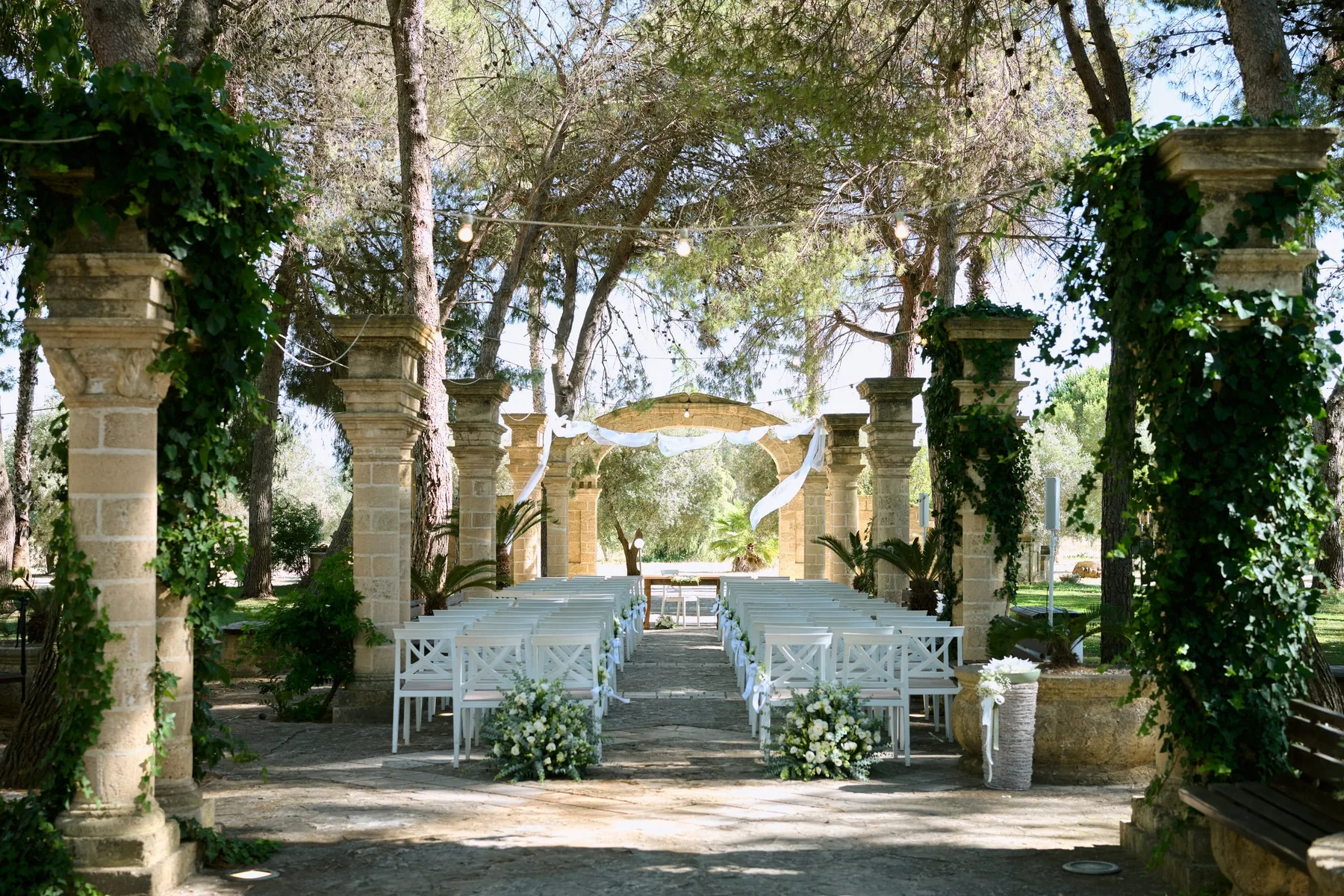 The ceremony avenue between stone columns and pine trees in the garden of Masseria Martuccio