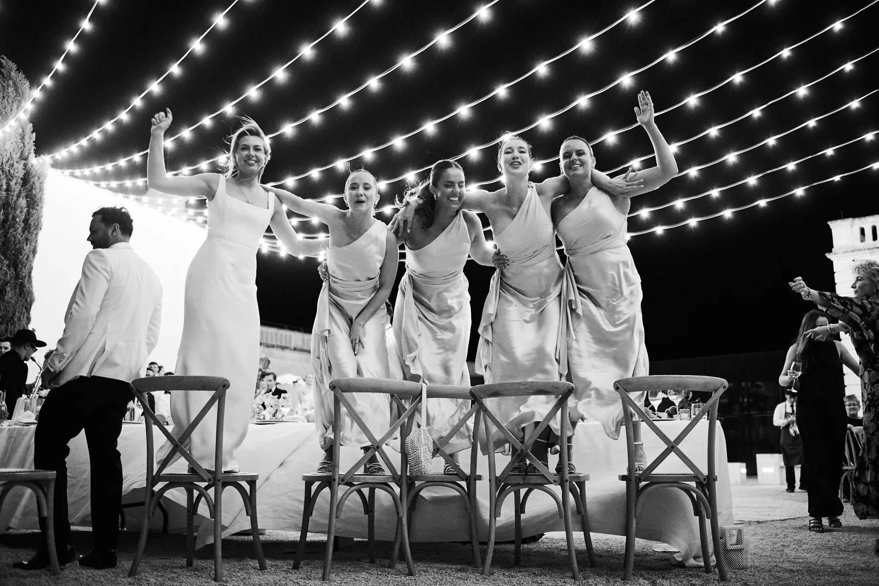 The bridesmaids dancing on the chairs, in black and white