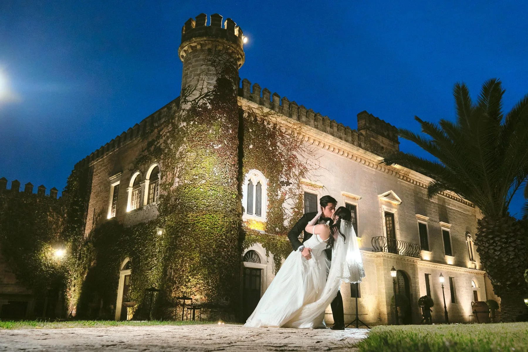 Castello Monaci illuminato la sera, con gli sposi in primo piano